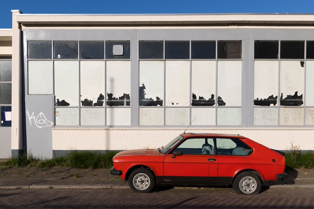 Röd bil med punktering parkerad framför en förfallen industribyggnad.